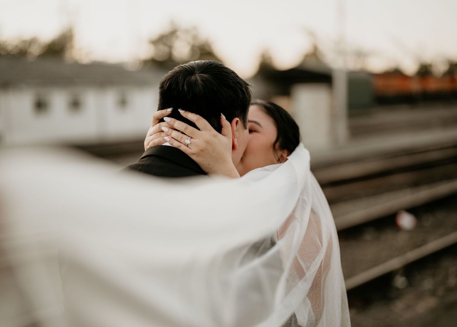 Asian husband and wife sharing a kiss by the train tracks on their wedding day in Seattle, Washington.