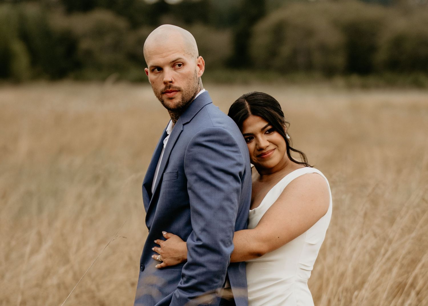 Husband and hispanic bride standing in a wheat field staring off into the distance in Seattle Washington