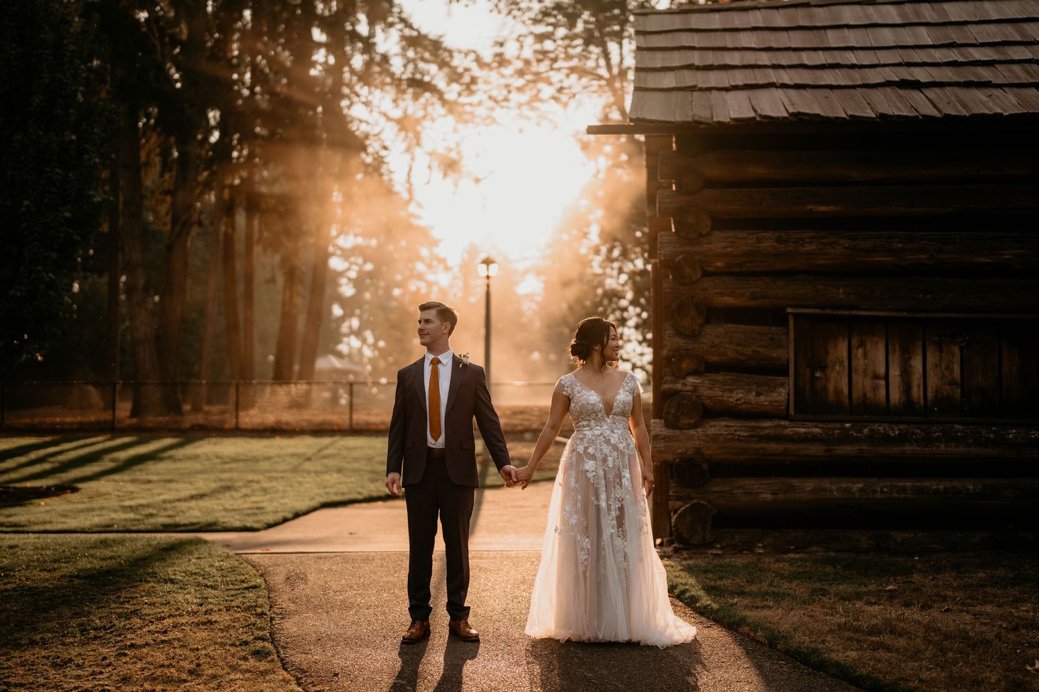 White and Asian husband and wife standing in front of the sun holding hands in Bellevue WA