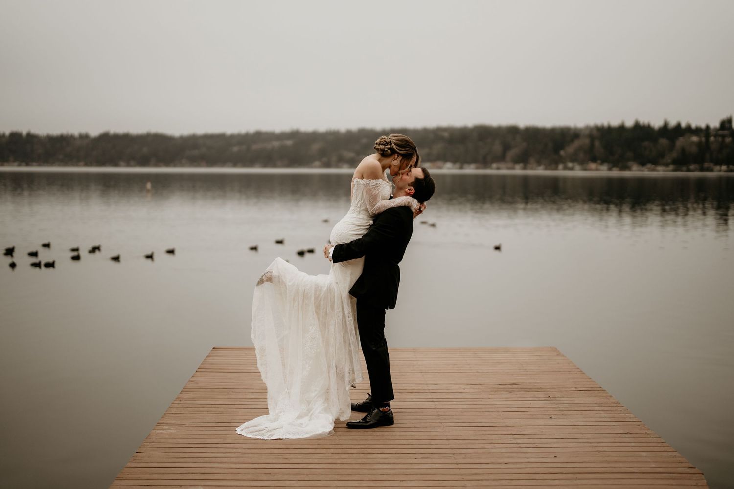 Husband lifting wife up on dock as they share a kiss in Seattle Washington for their first look. Wedding in Seattle Washington.