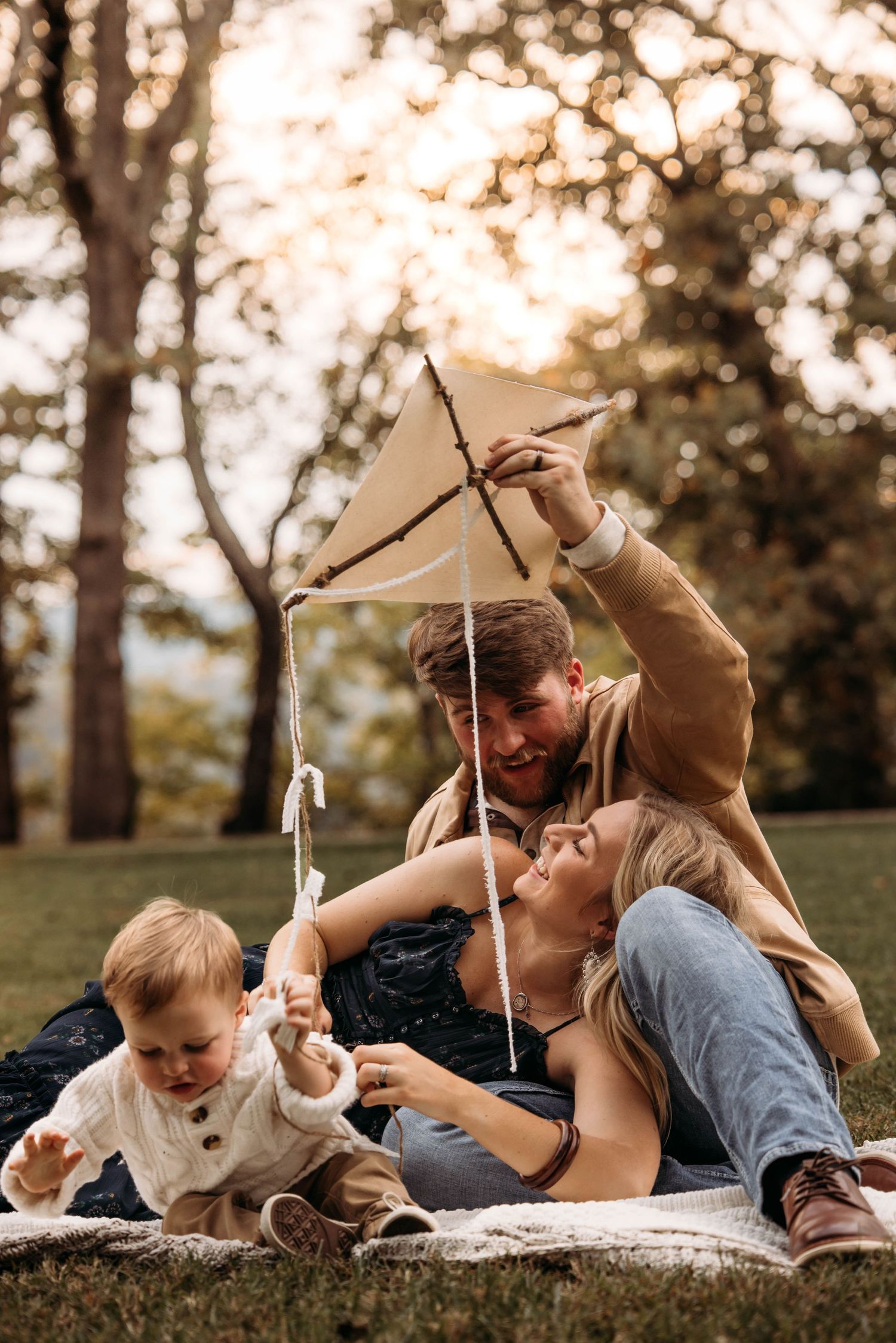 Young family playing with a handmade stick kite during a lifestyle photo session in a Branson, Missouri park at sunset.