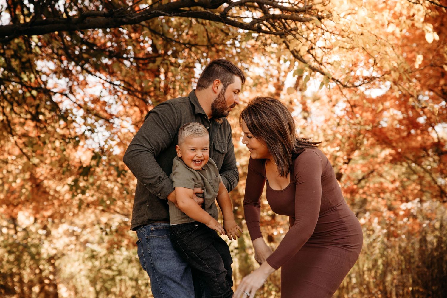 Young family laughing together during a fall photo session in the autumn woods of Branson, Missouri.