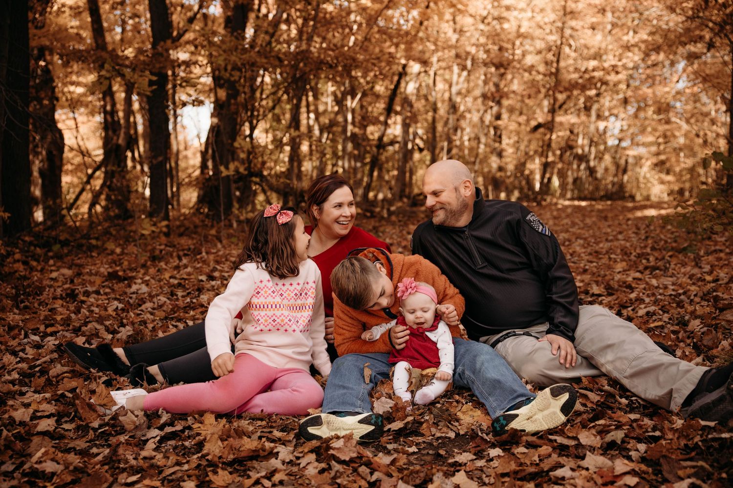 Family of five sitting in autumn leaves during a fall photo session in the Branson, Missouri woods.