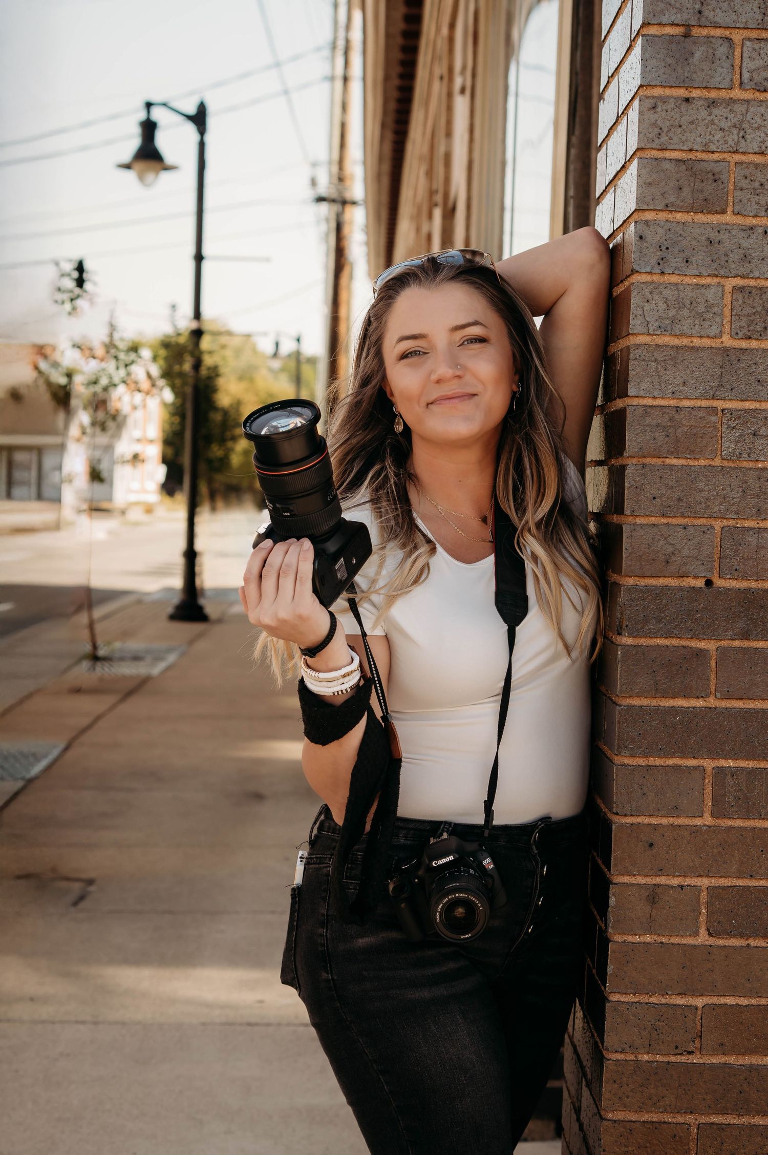 Professional photographer L. Ballenger smiling and leaning against a brick wall during a photo session in the Ozarks.