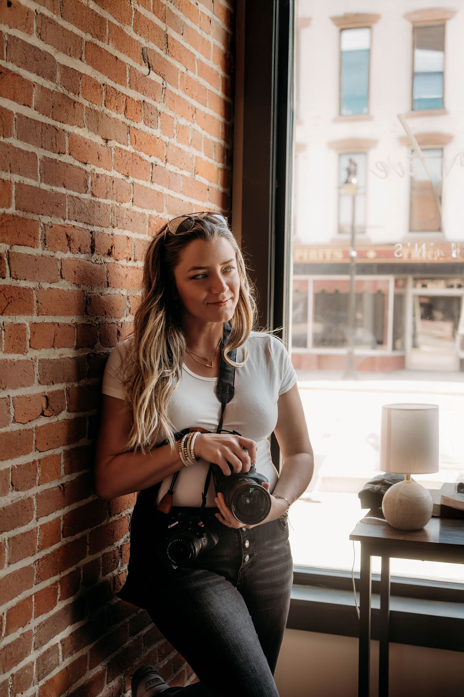 Professional Branson, MO Photographer L. Ballenger holding her camera while leaning against a rustic brick wall in Downtown Branson.