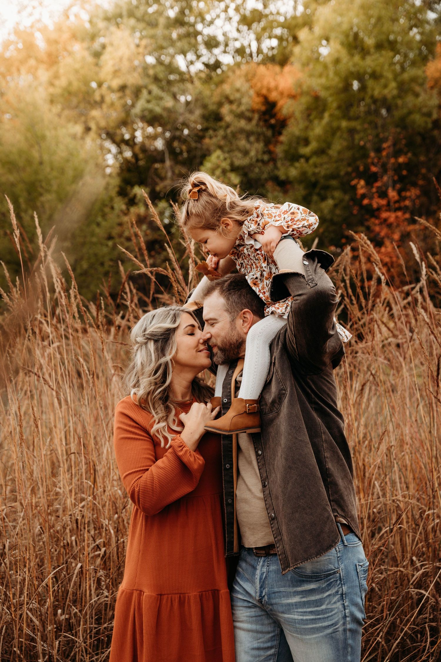 Young family of three sharing an intimate moment in a field of tall grass during a fall photo session in Branson, Missouri.