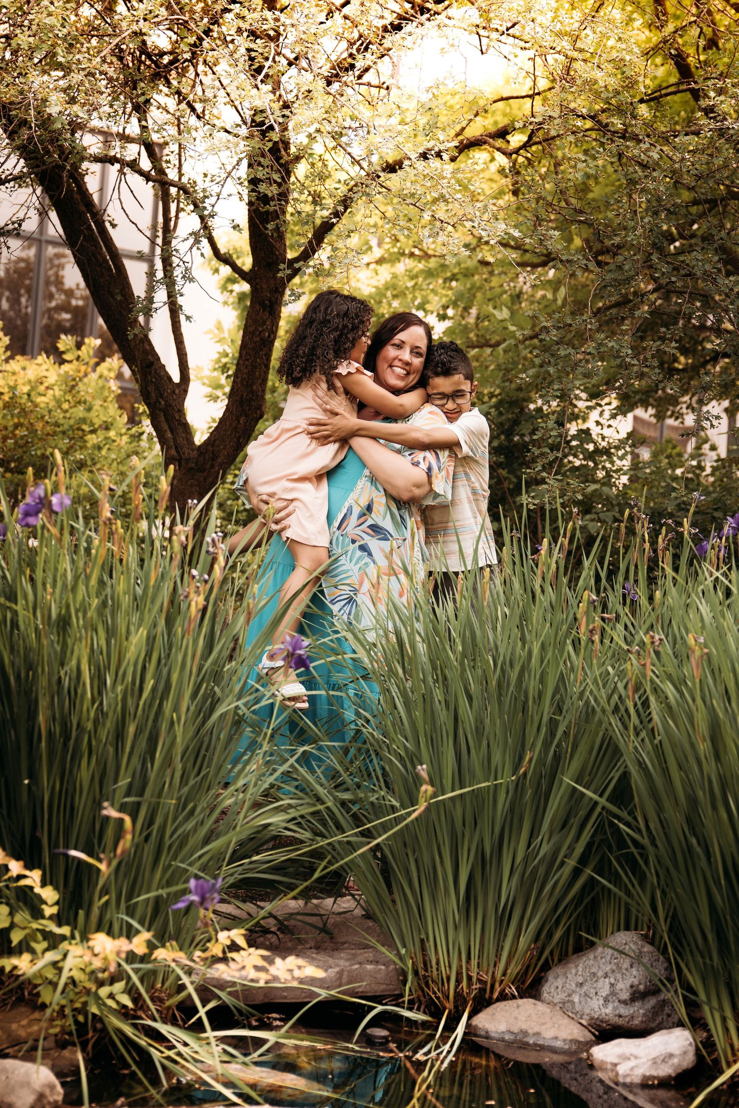Mother hugging her two children in a garden of purple irises during a summer photo session in Branson, MO.