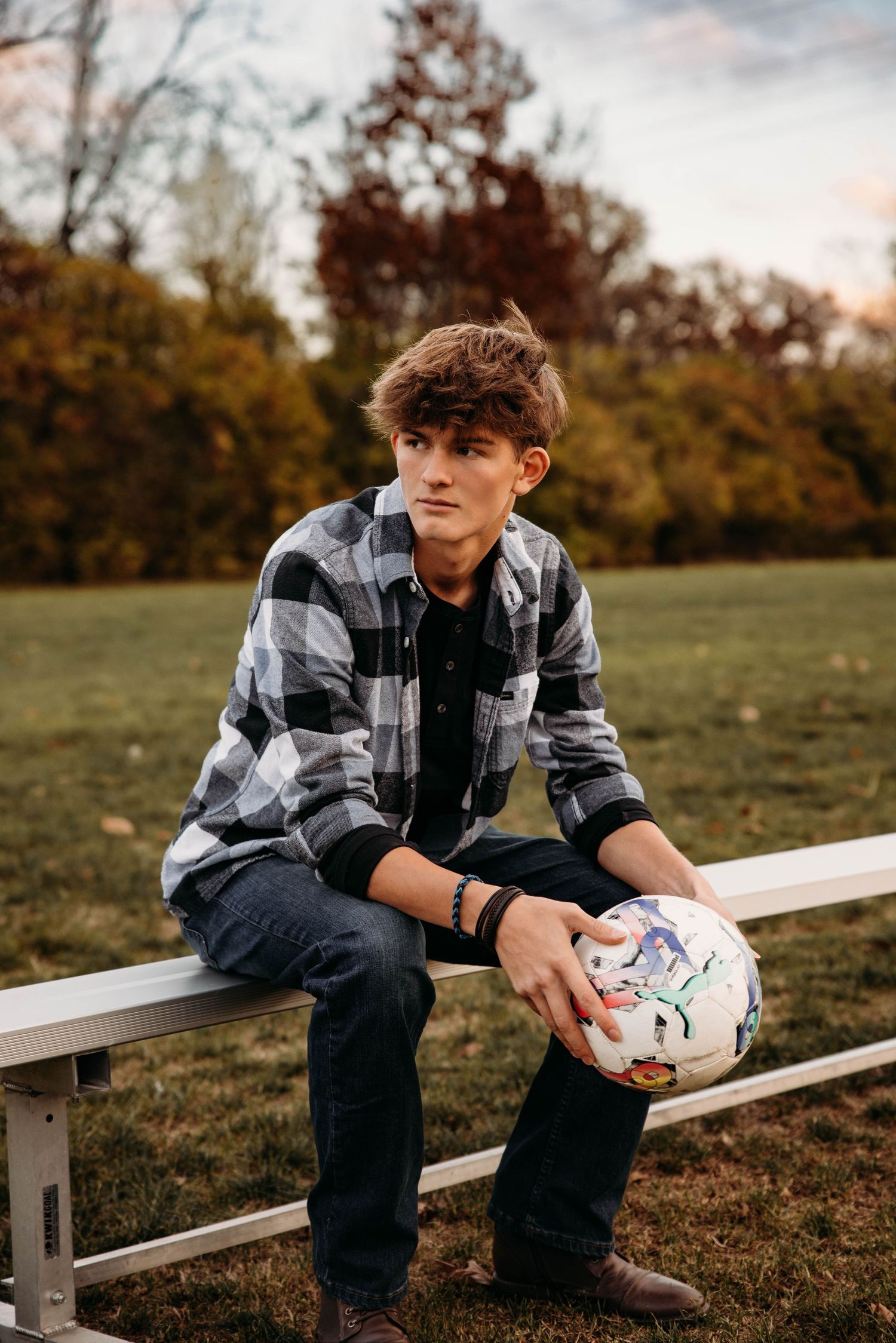 High school senior sitting on a bleacher holding a soccer ball during a fall photo session in Branson, MO.