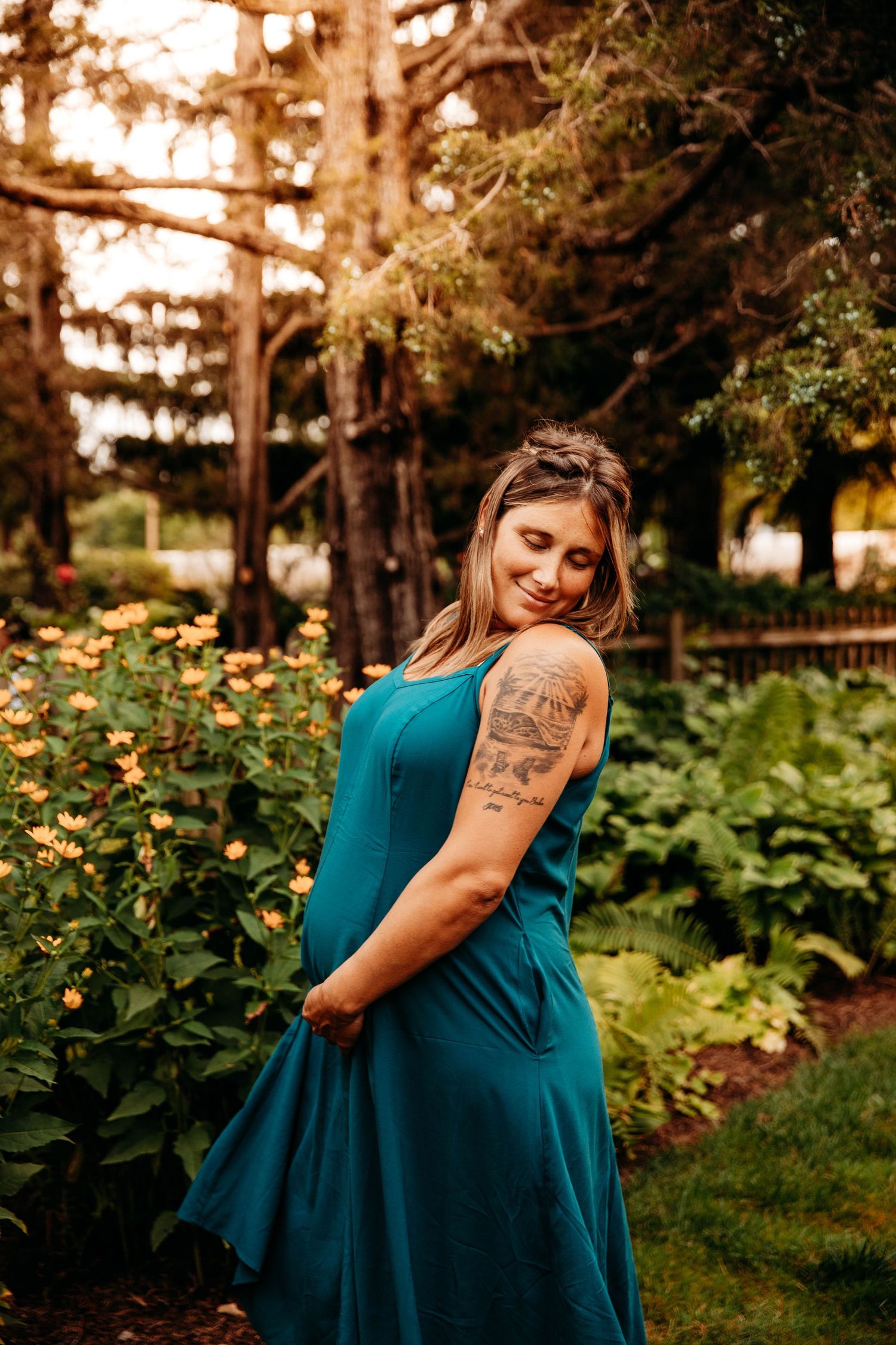Pregnant woman in a teal blue dress smiling in an outdoor garden during a maternity photo session in Branson, MO.