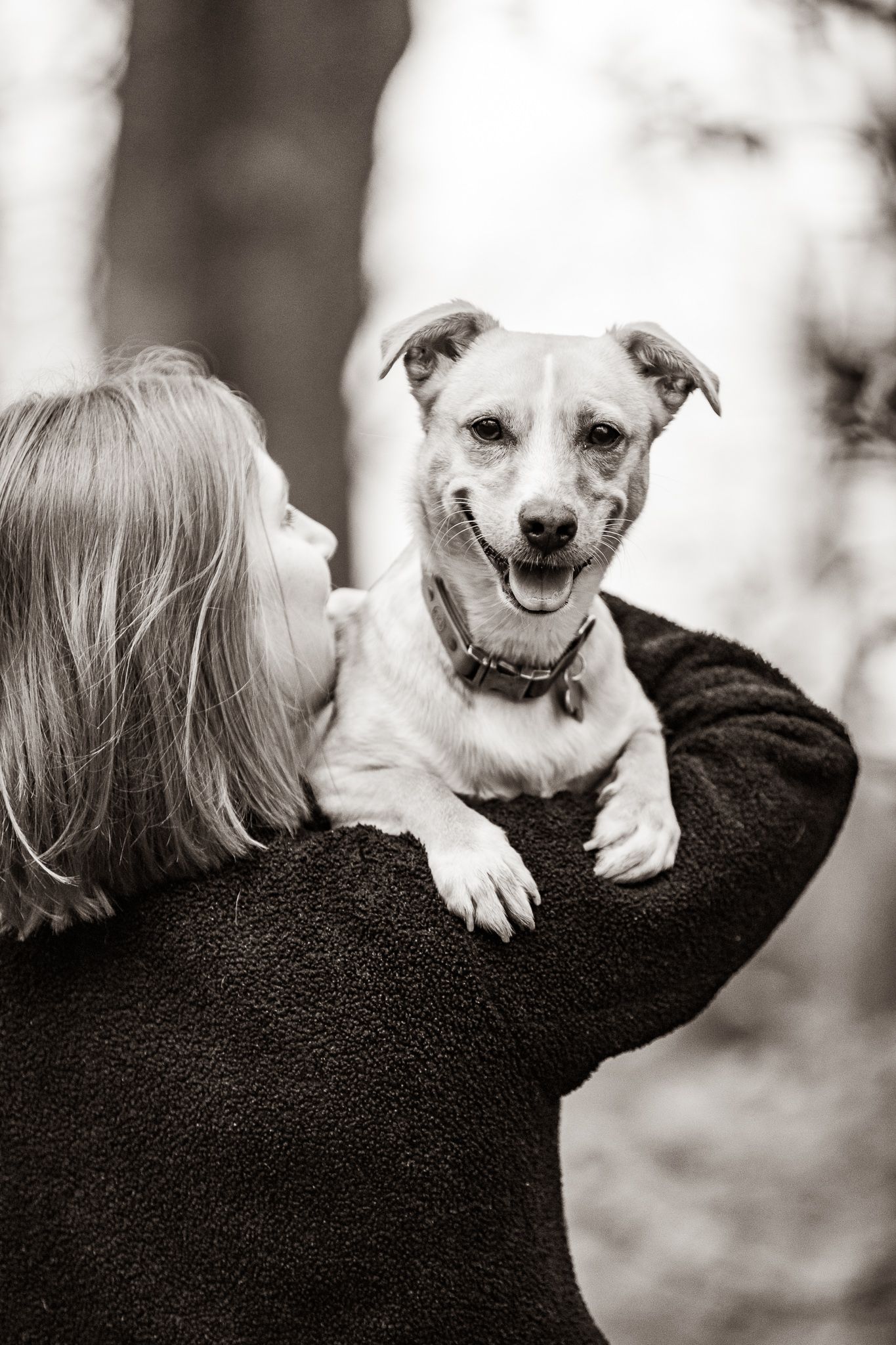 Happy tan and white rescue dog being held on shoulder in black and white portrait.