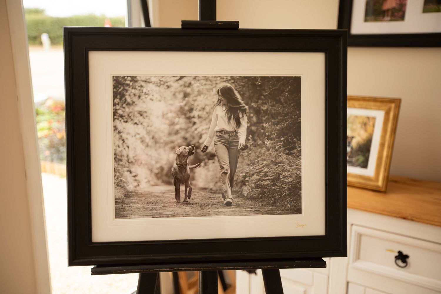 A gallery wall displays multiple black and white photographs in wooden frames against a white wall.