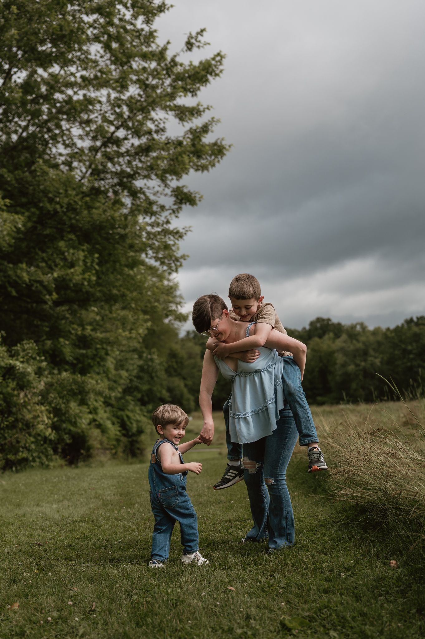 Playful family moments captured in a grassy field under moody storm clouds.