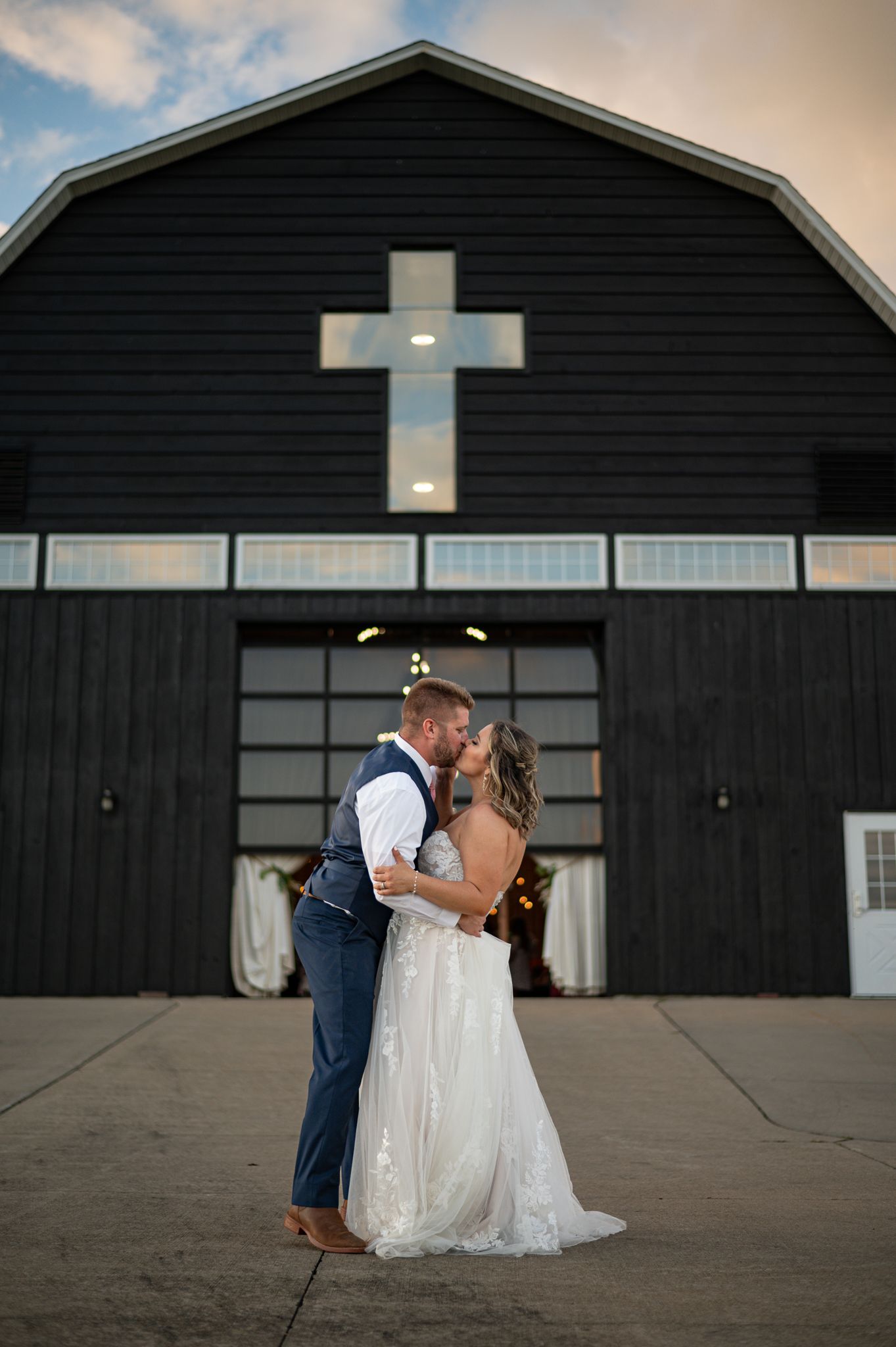 Wedding portrait in front of modern black barn with illuminated cross at sunset in Stark County, Ohio.