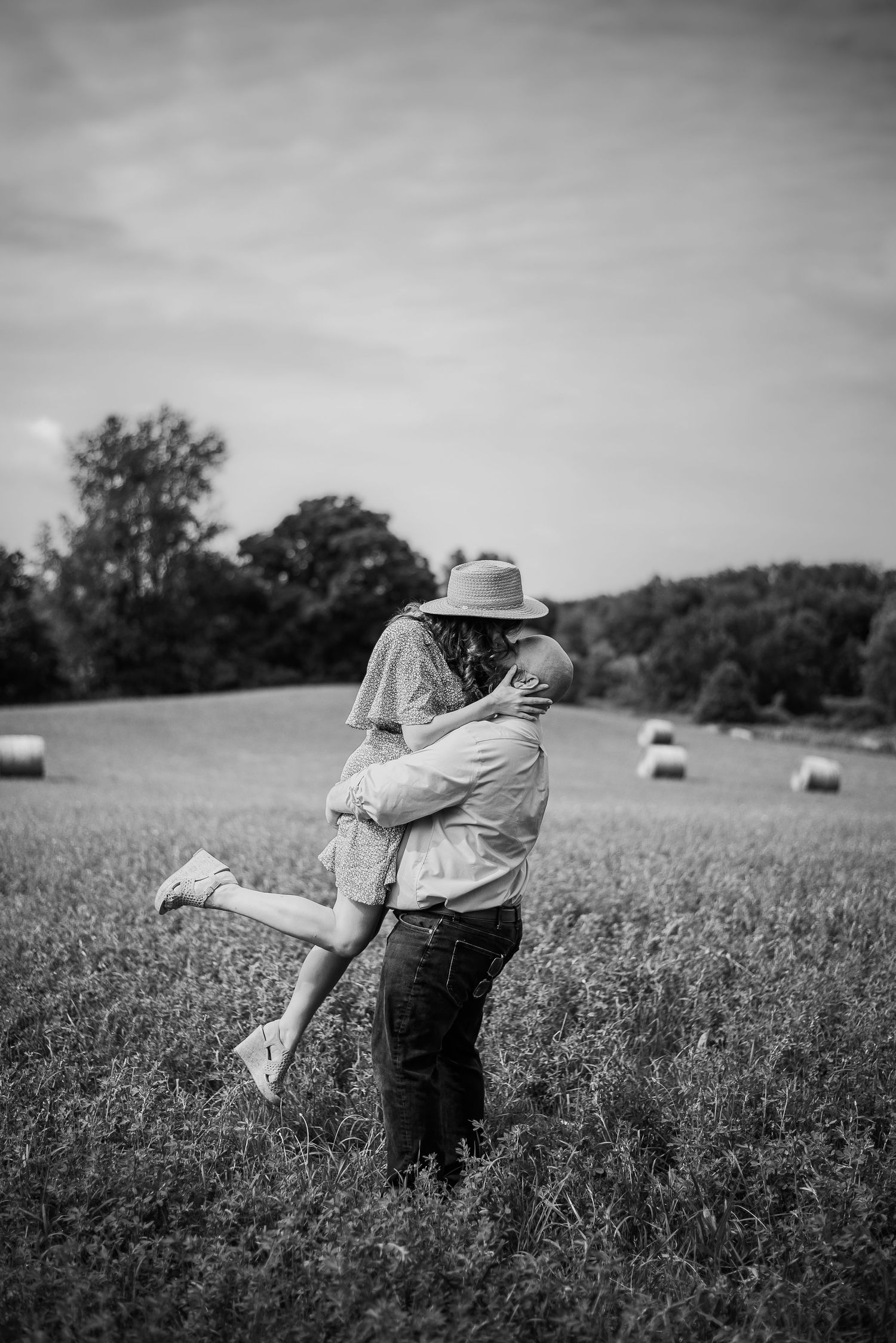 Black and white photo series of a couple dancing playfully in a field with hay bales.