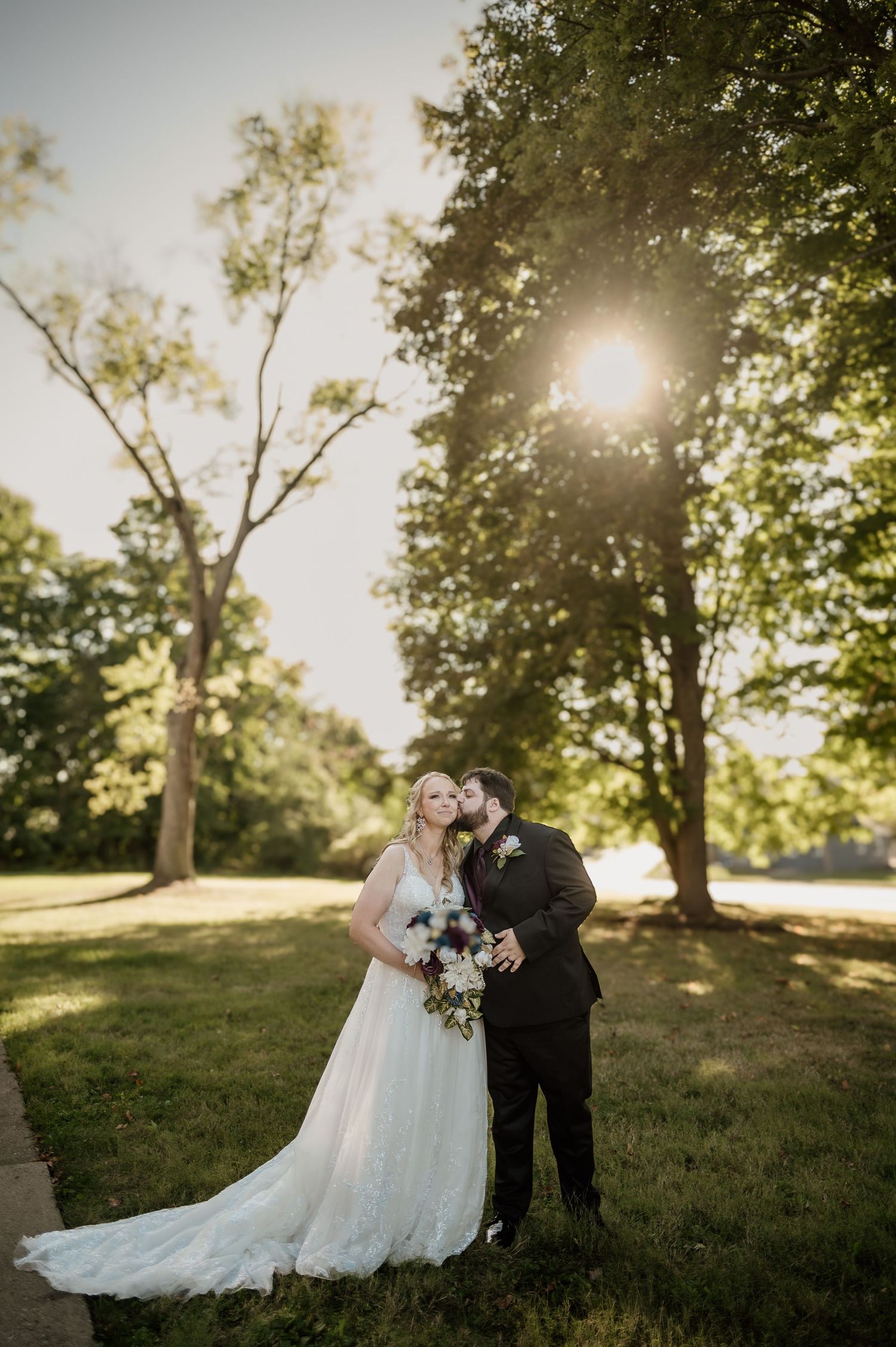 A couple shares a romantic moment in a sunlit meadow surrounded by trees during their wedding photoshoot.