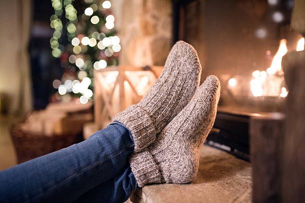 Cozy wool socks warming by a fireplace with Christmas lights twinkling in the background.