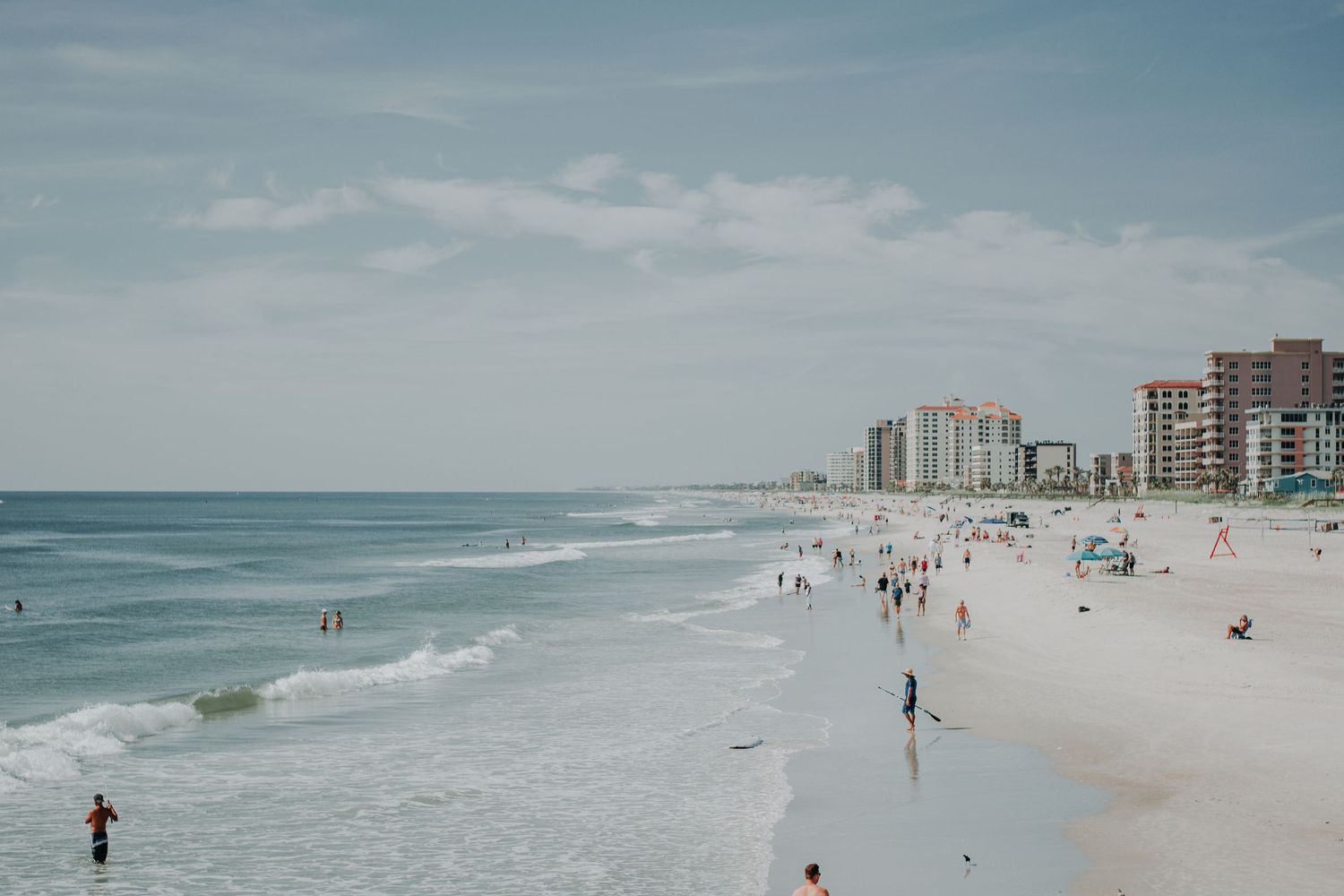 Panoramic view of a sandy beach with high-rise buildings, beachgoers, and rolling waves along the coastline.