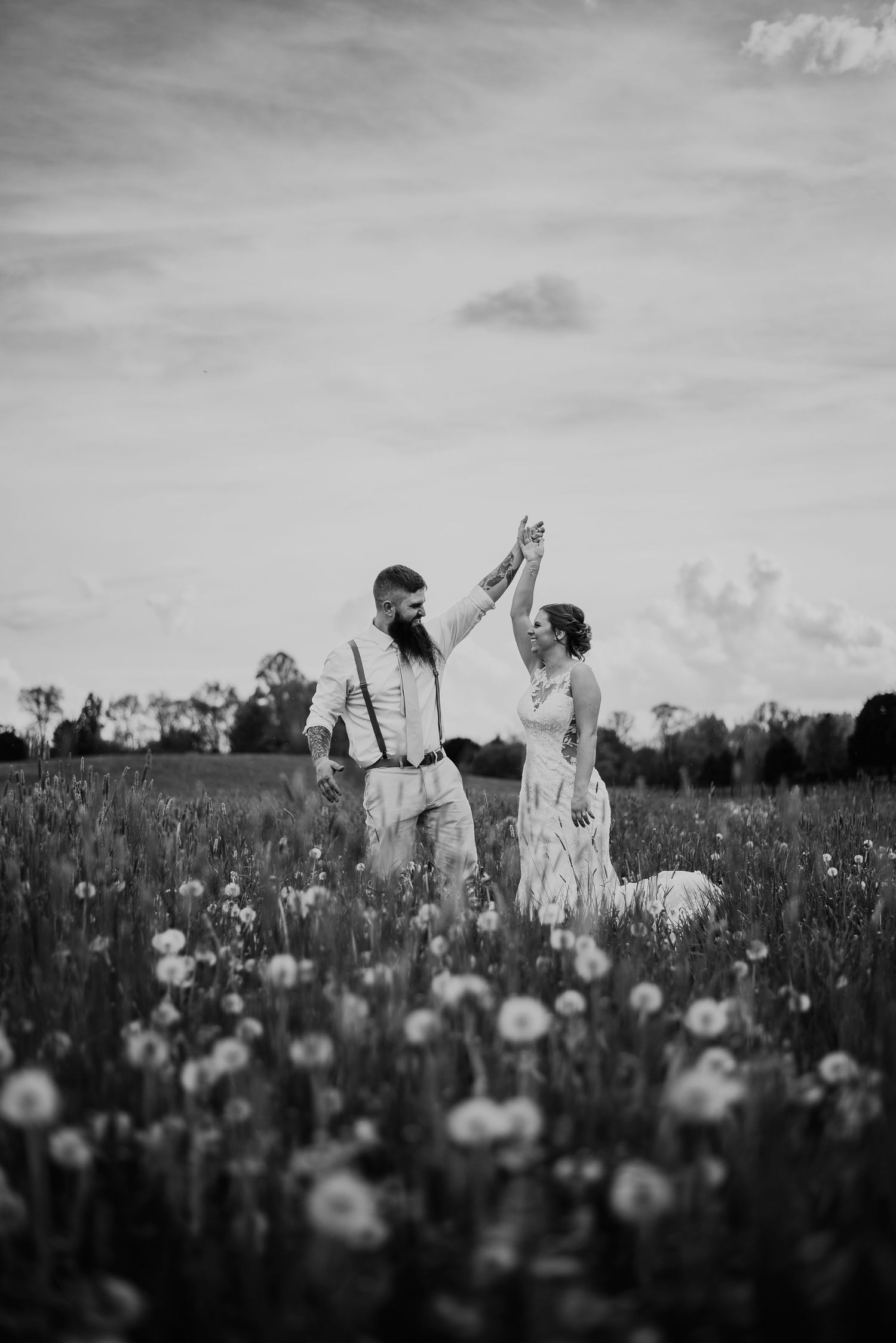 A black and white portrait of a bride and groom dancing in a field of dandelions.