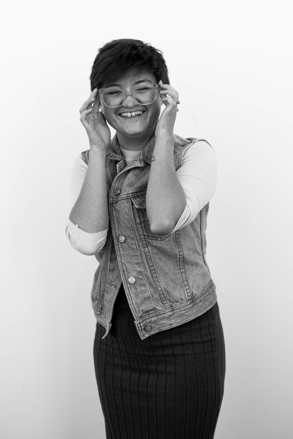 A black and white portrait of someone wearing a denim vest and glasses against a white background.