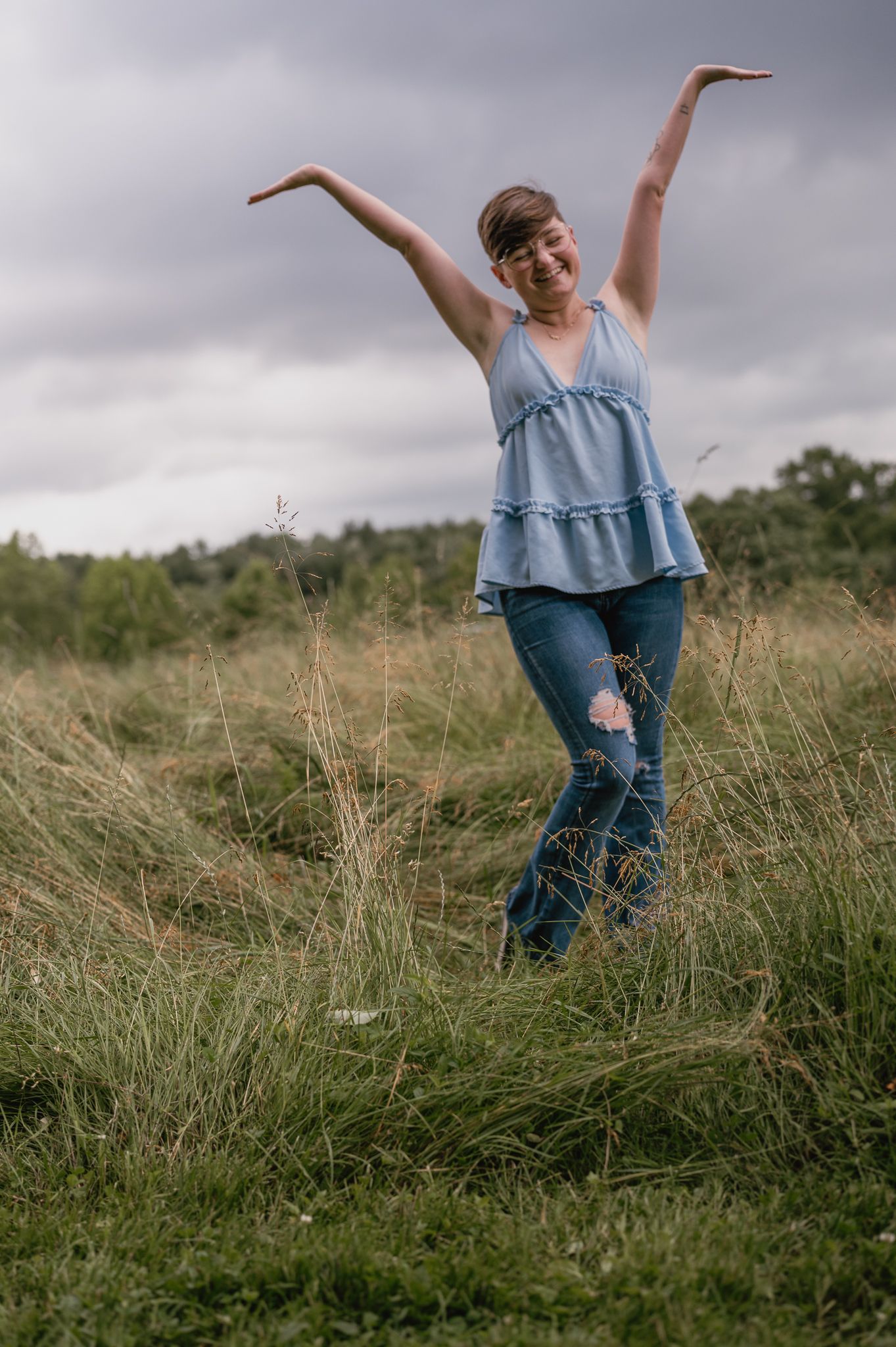 A joyful figure dances freely in a wild grass field under dramatic cloudy skies.