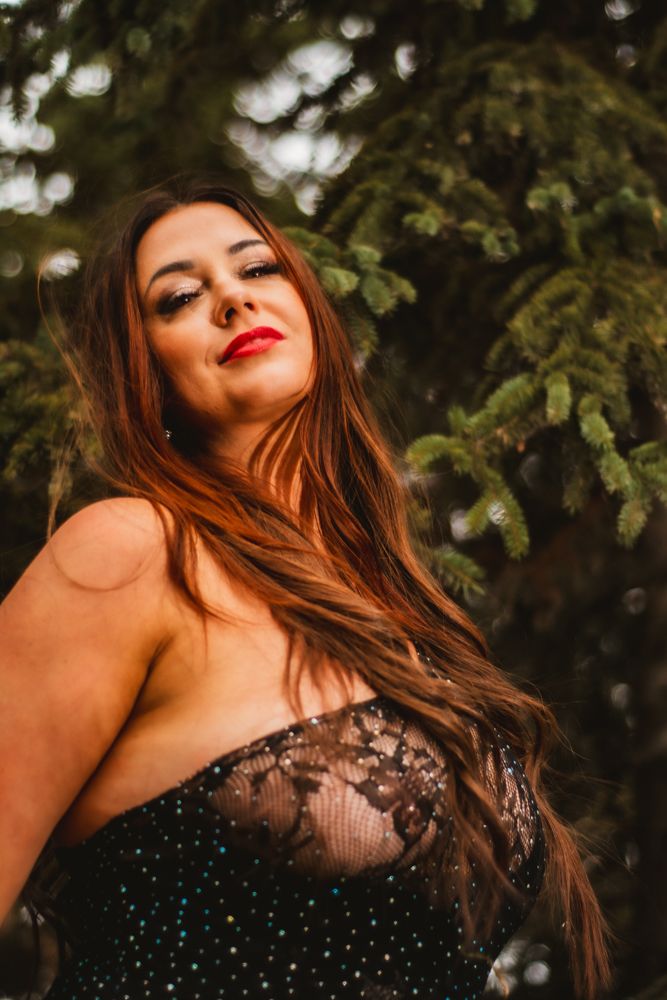 Dramatic portrait with long hair and lace dress against forest greenery.