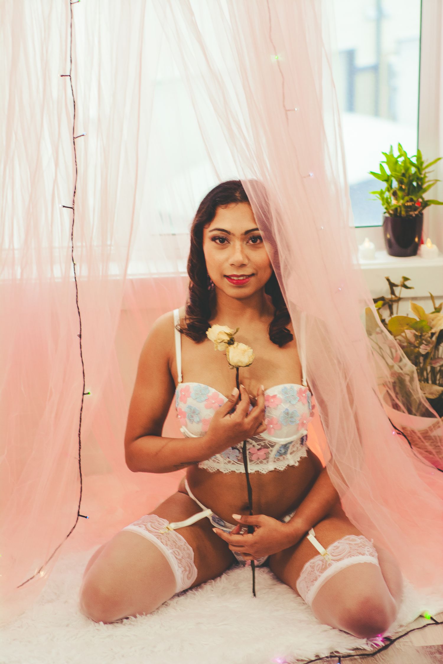 Boudoir photography against pink backdrop with decorative plants and white roses.