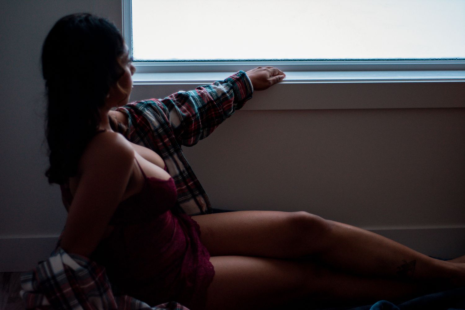 Moody silhouette of person reclining by window in intimate indoor photoshoot.