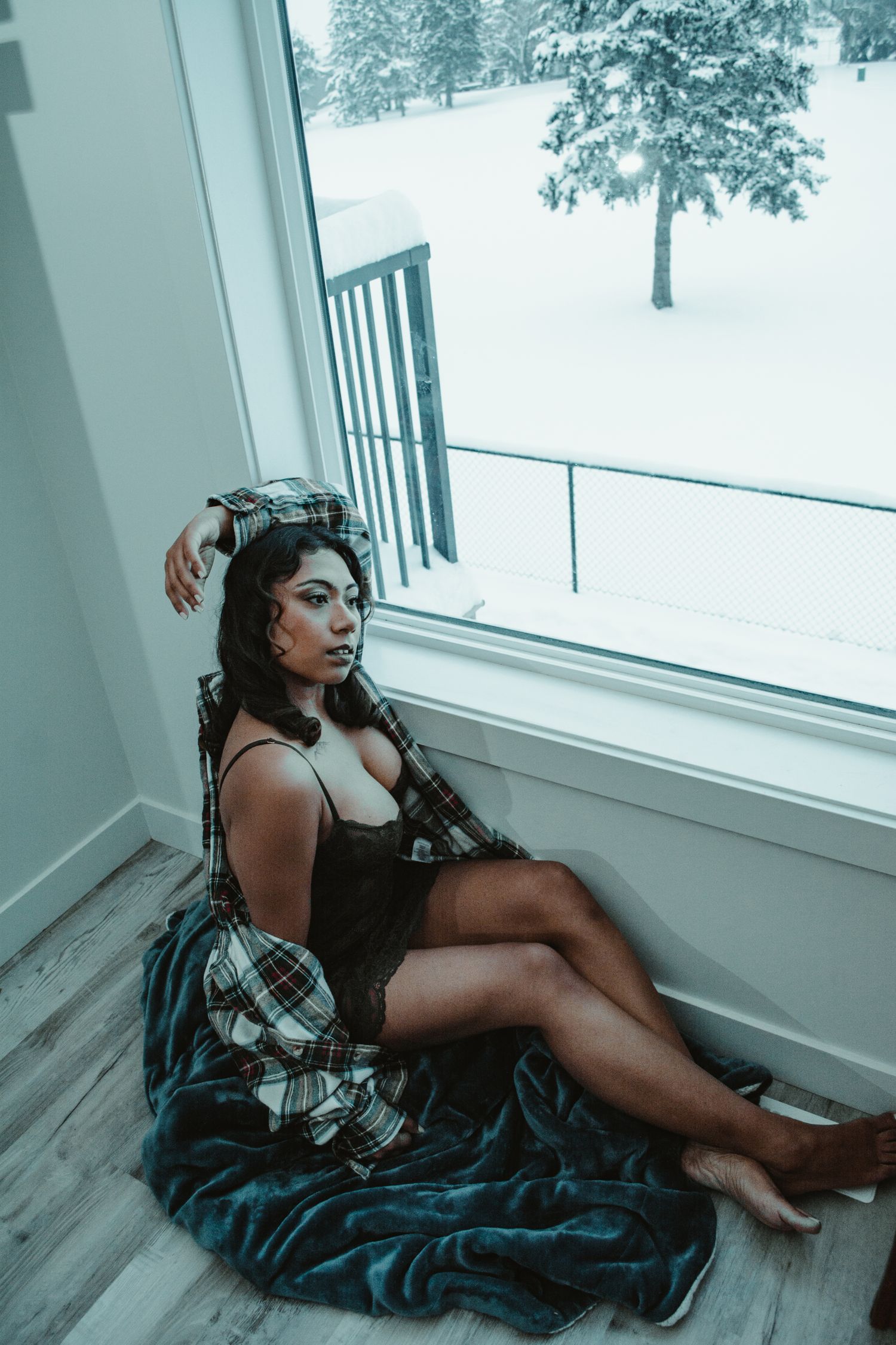 Moody portrait of person resting by window overlooking snowy winter landscape.