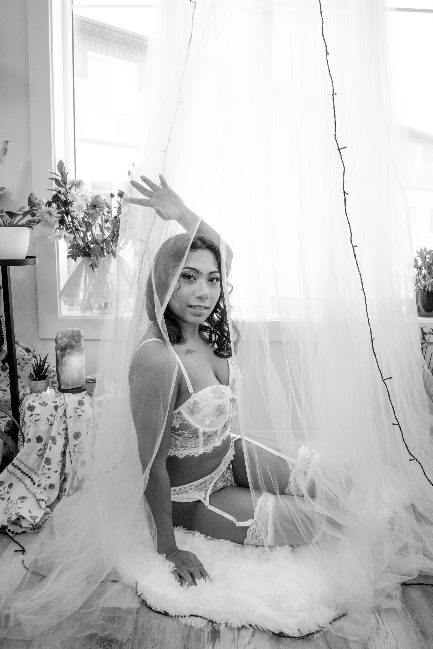Artistic black and white boudoir portrait with flowing white tulle and natural window light.
