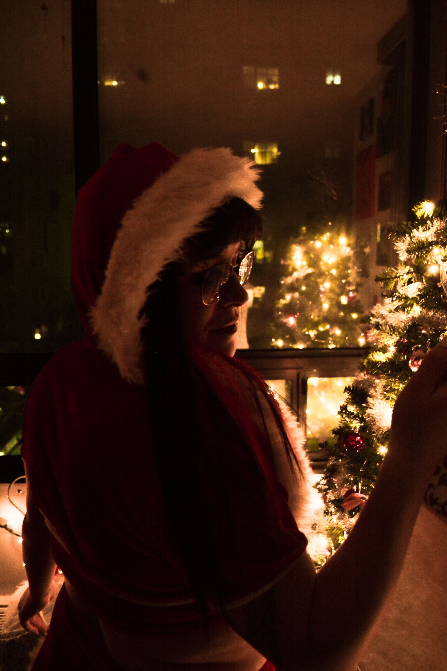 A dimly lit holiday scene with someone adjusting decorations on a Christmas tree.