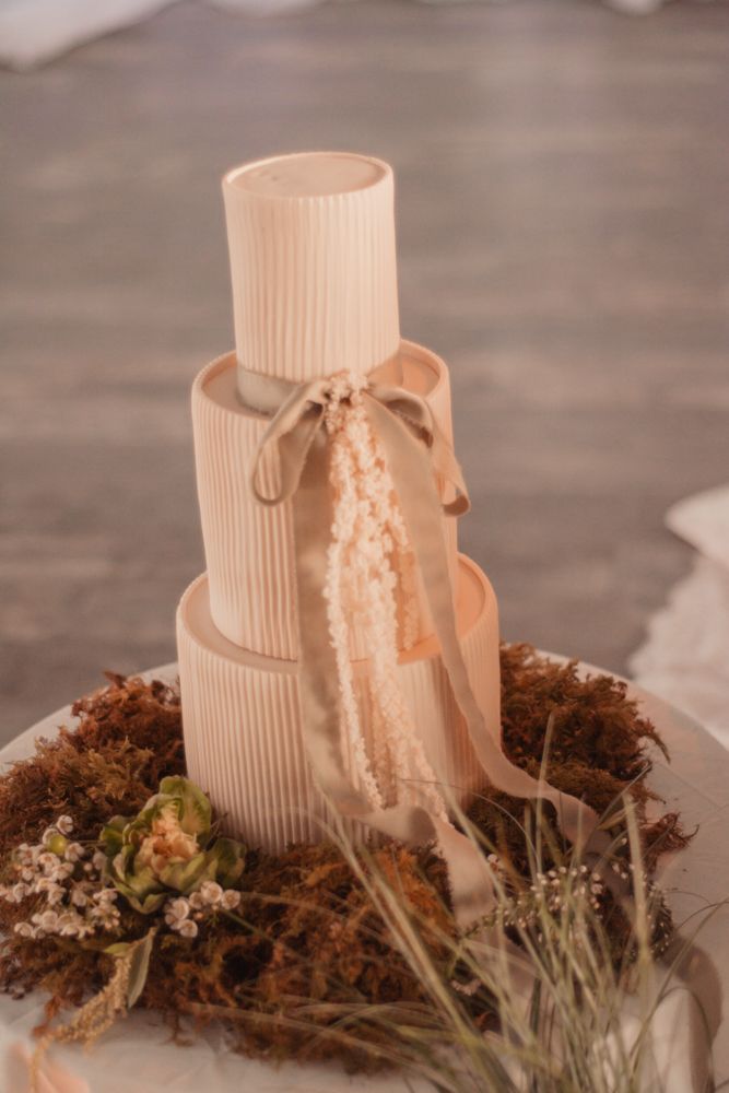 Three-tiered cream-colored wedding cake decorated with ribbons and dried flowers.