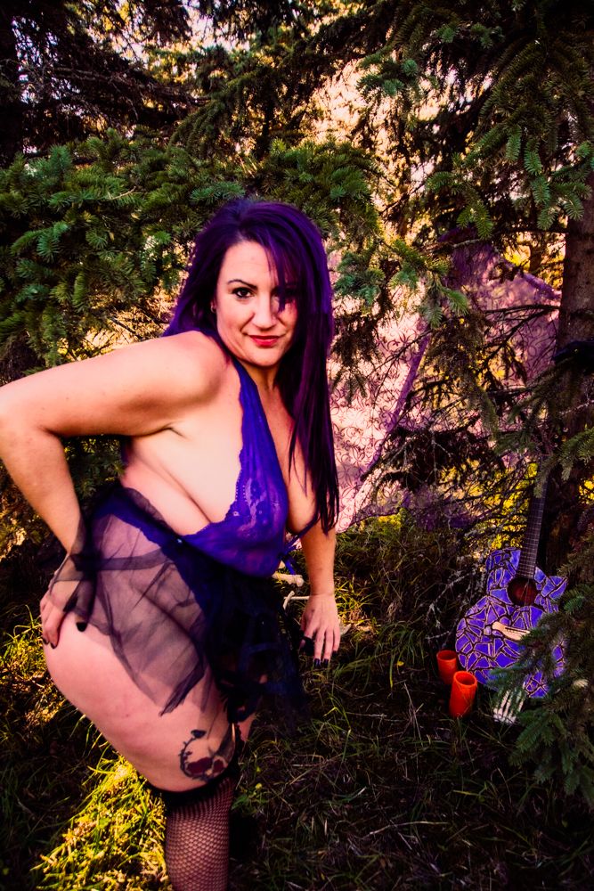 Purple and black gothic costume against magical forest backdrop with Halloween decorations.