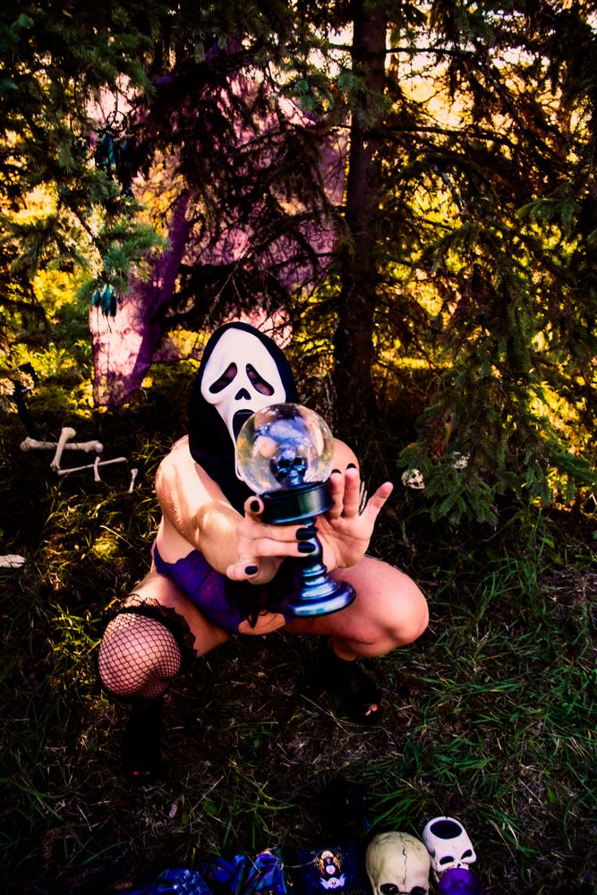 Haunting Halloween scene with crystal ball, ghostly mask, and eerie decorations in twilight forest setting.