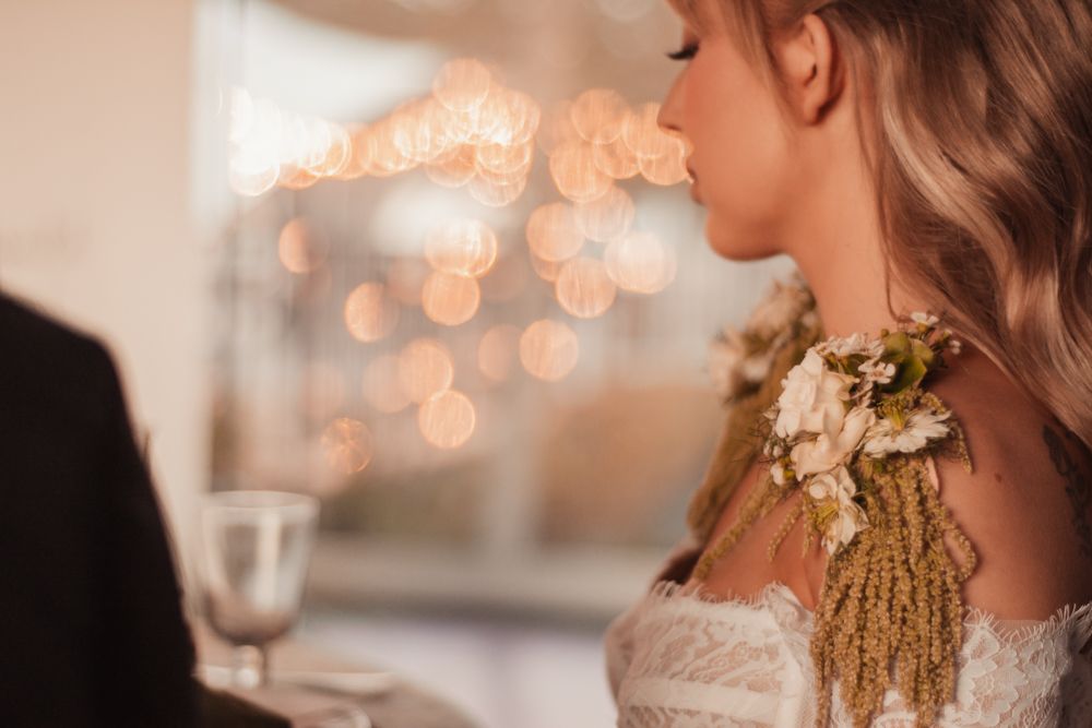 Romantic wedding detail shot with bokeh lights and floral shoulder accessories.