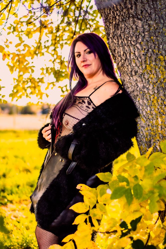 Autumn fashion portrait with black coat and fishnet details against golden foliage.