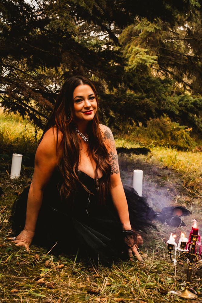 A gothic photoshoot in a forest setting with red smoke and candles features a corset dress and autumn scenery.