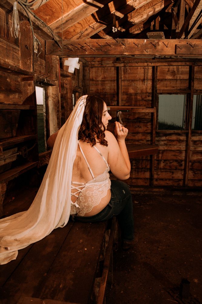 Intimate portrait in rustic barn interior with flowing white fabric and wooden details.