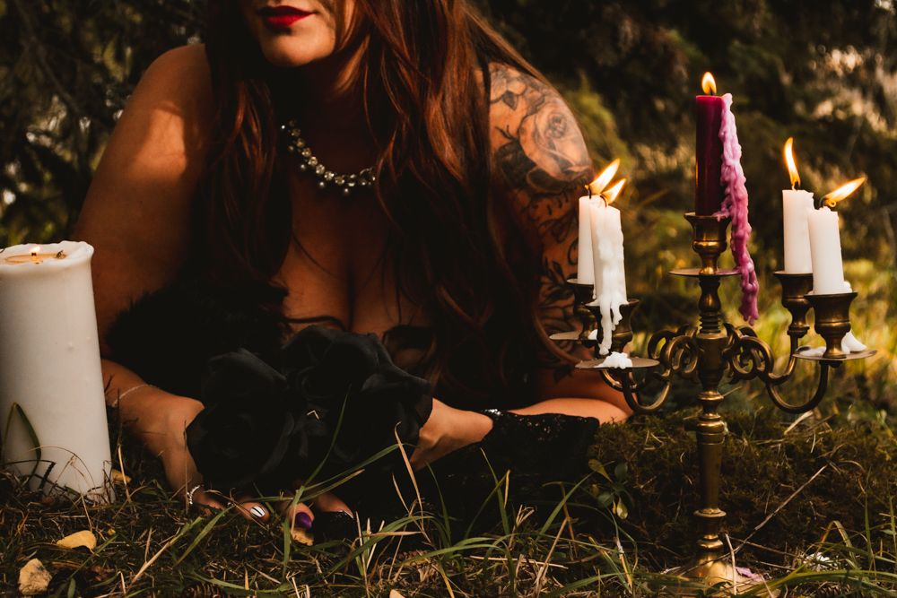 Artistic shot of candles and black dress details against forest ground.
