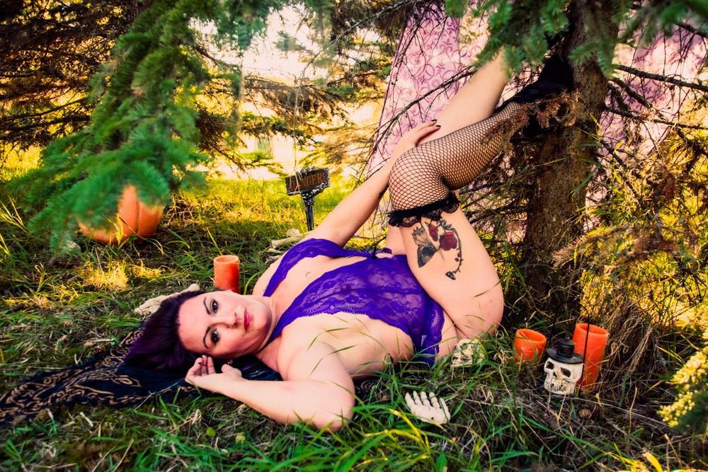 Spooky Halloween boudoir photo with gothic decorations and natural lighting in forest setting.