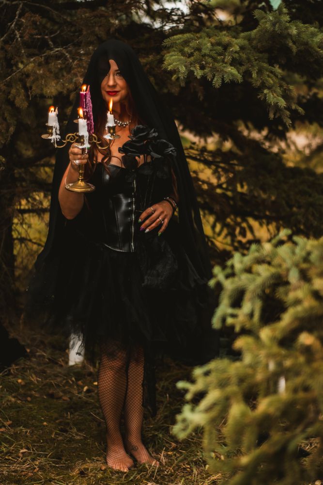 Dark atmospheric photo of figure in black dress holding candelabra in forest.
