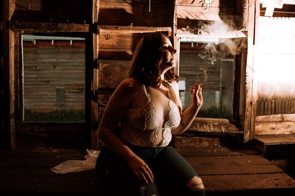 Artistic boudoir portrait in atmospheric barn setting with vintage wooden details.