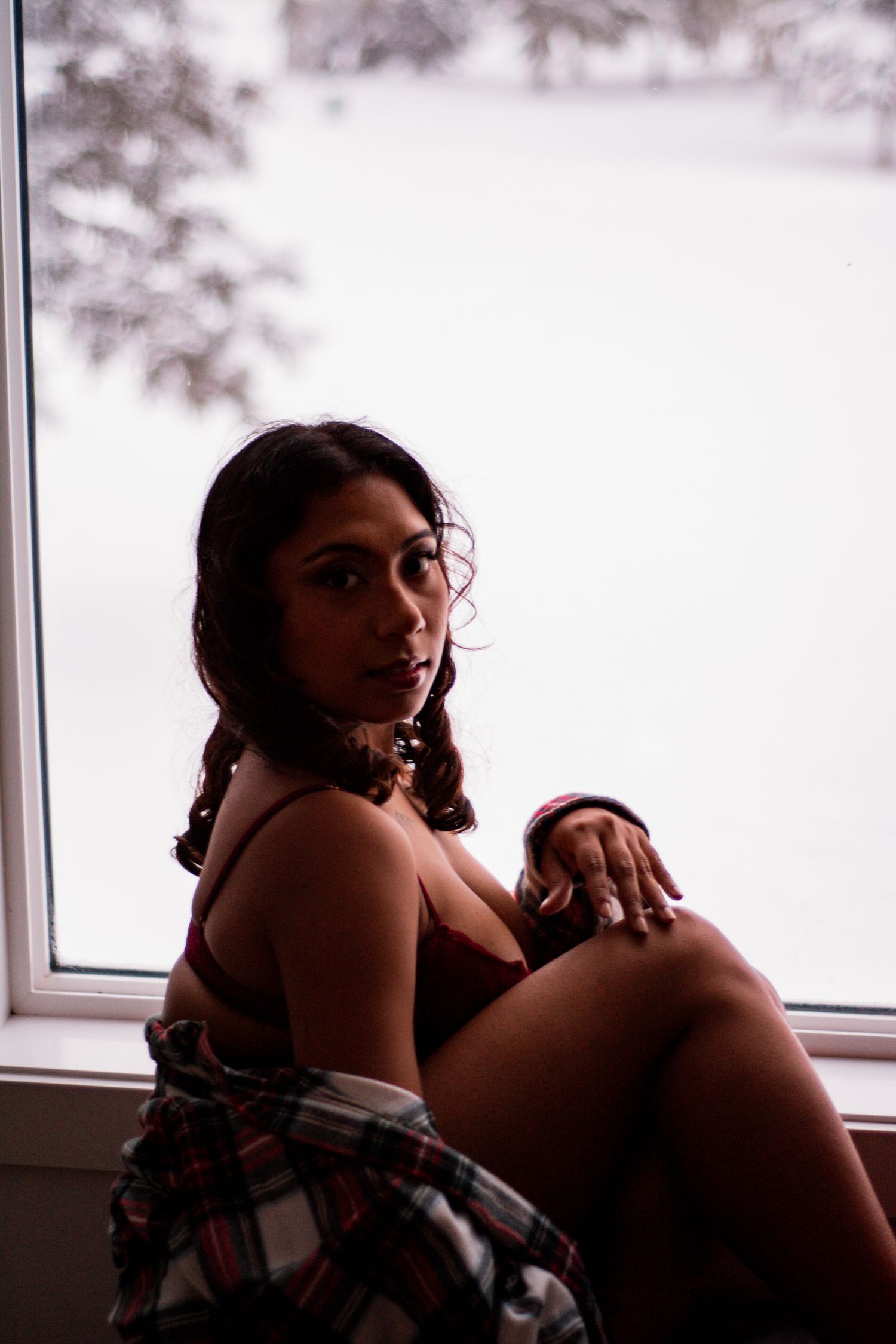 Intimate portrait in red lingerie and plaid wrap by window with winter scene.