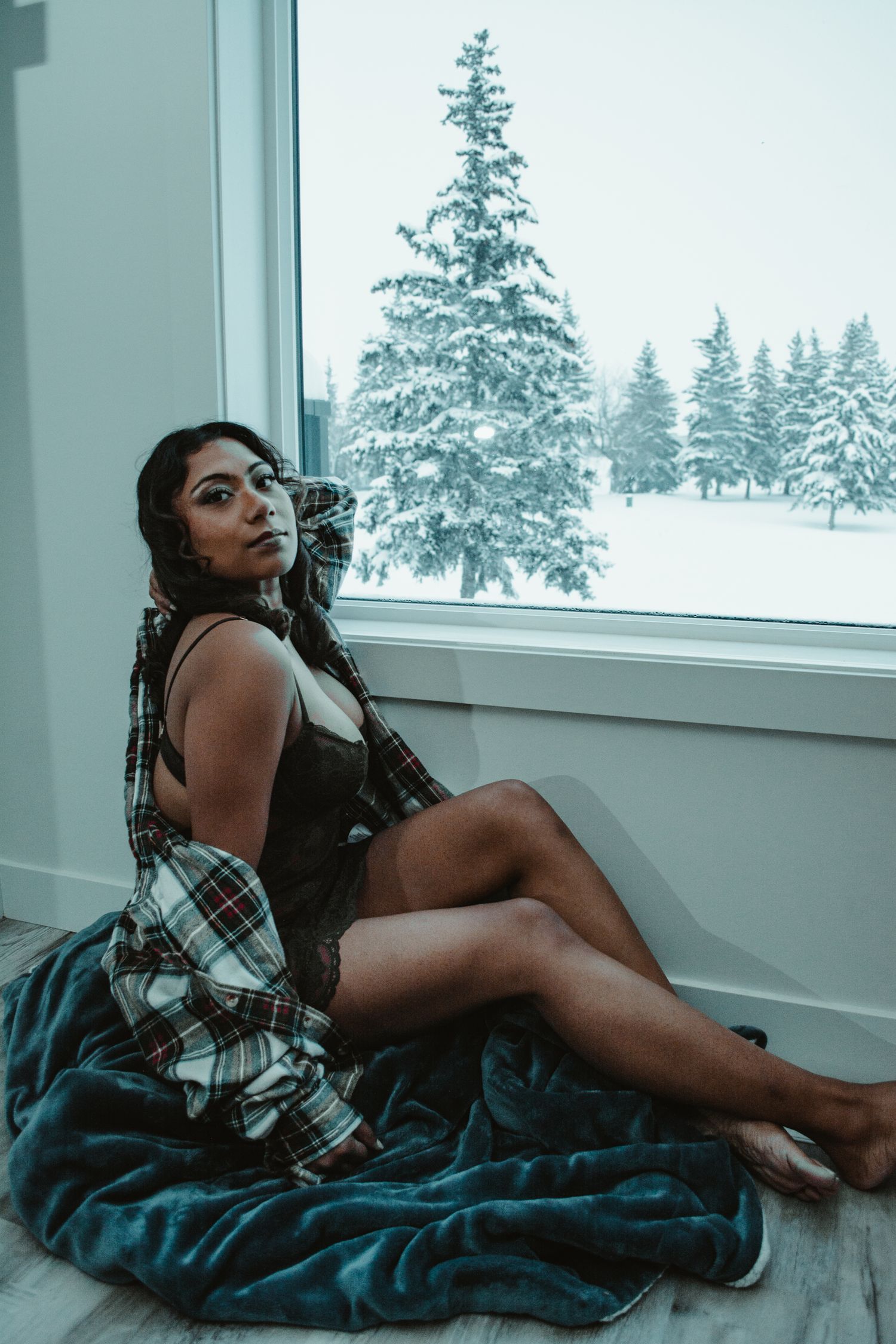 Intimate portrait session with snow-covered pine trees visible through large window.