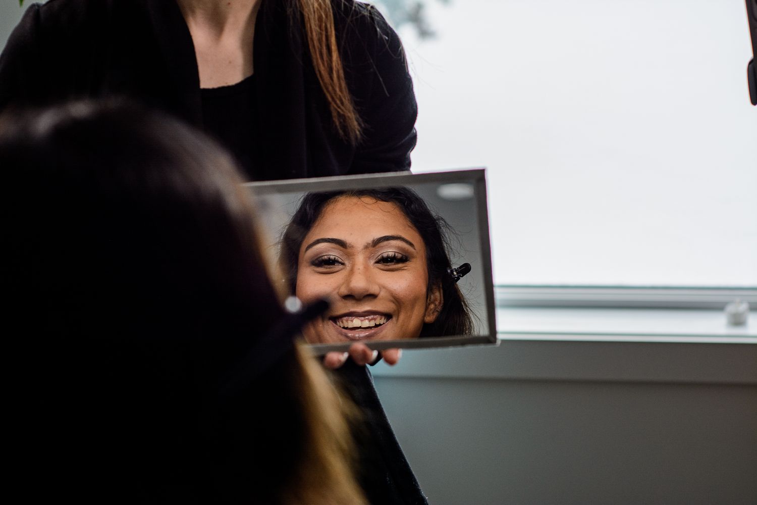 Reflection in makeup mirror shows someone smiling during professional beauty session.