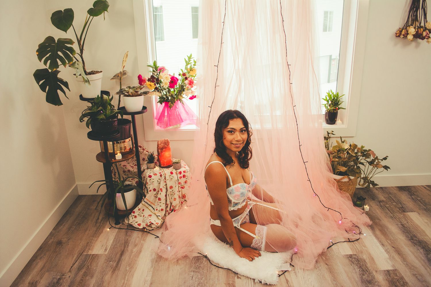 Romantic boudoir portrait with pink tulle backdrop and floral decorations in natural window light.