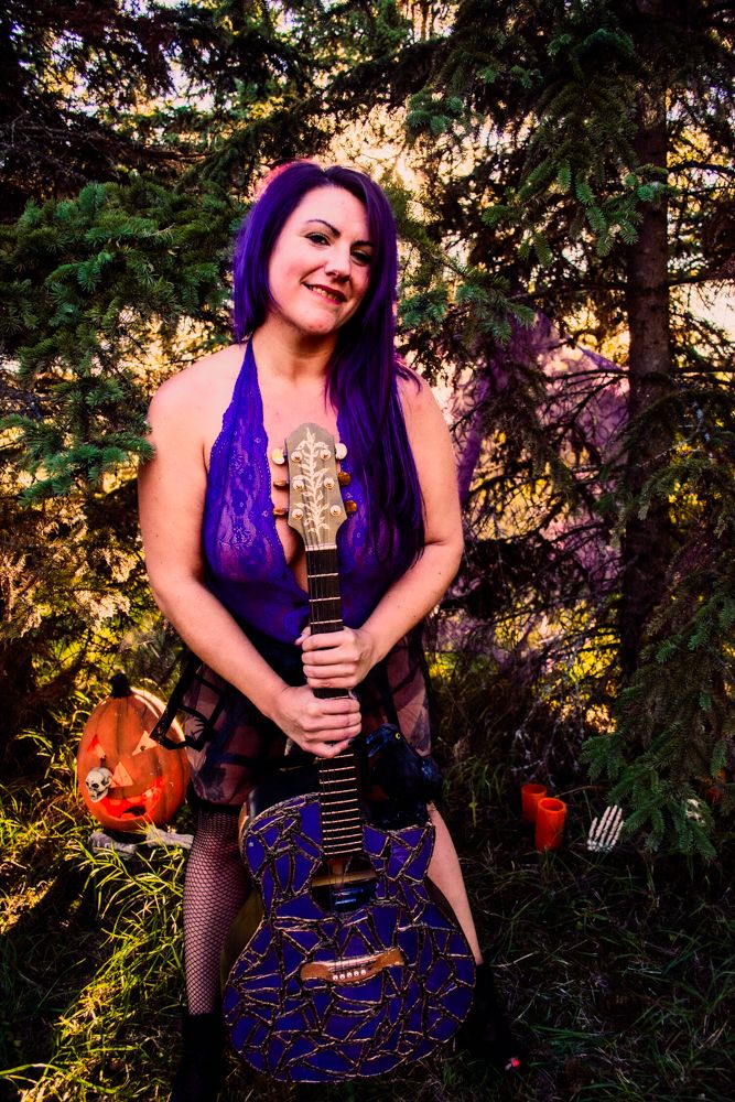 Alternative styled musician poses with a unique purple and black crackle-design electric guitar outdoors.