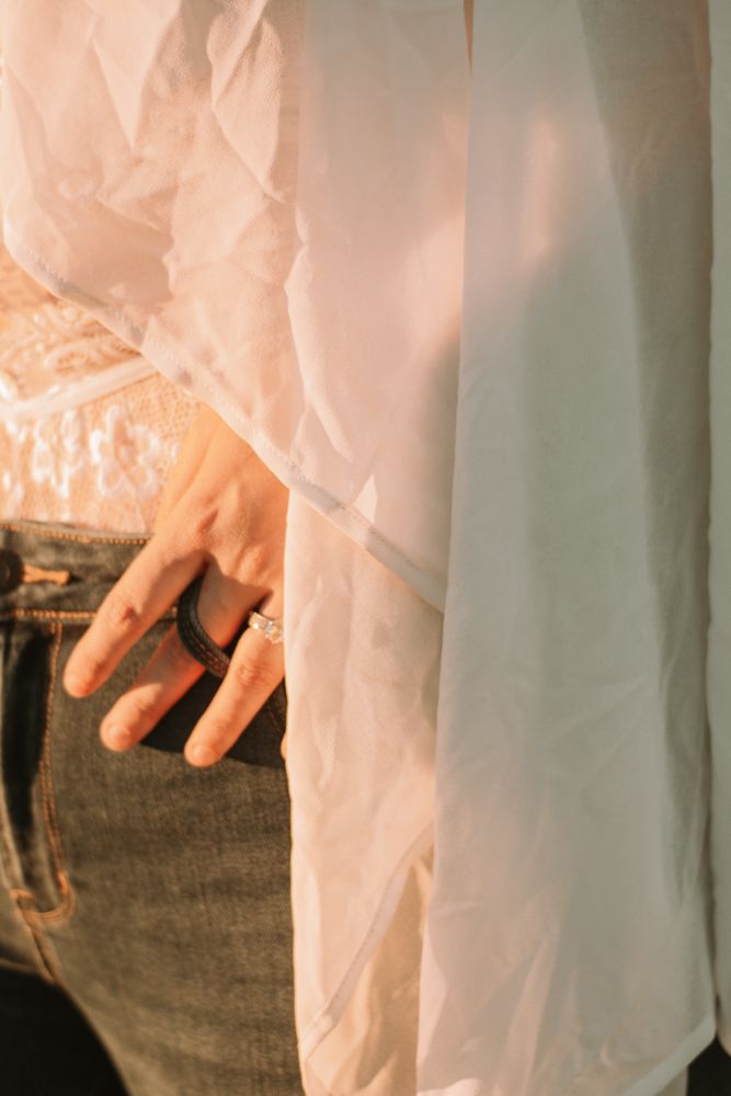 Detail shot of hand against jeans with sheer white fabric in warm lighting.