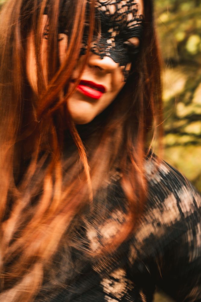 Close-up portrait with lace mask, red lipstick and autumn forest backdrop.