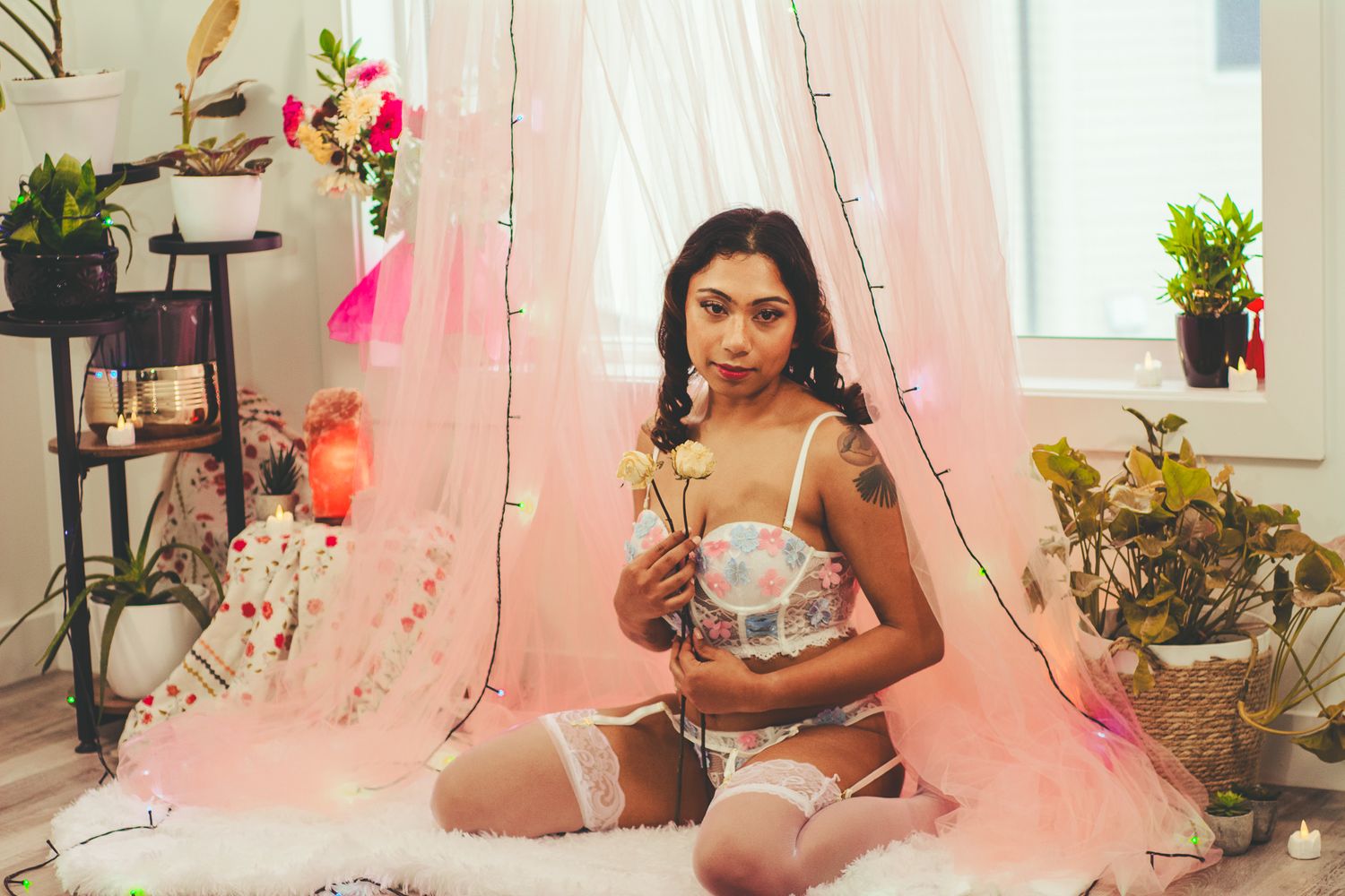 Romantic portrait in lingerie surrounded by pink curtains and potted flowers.