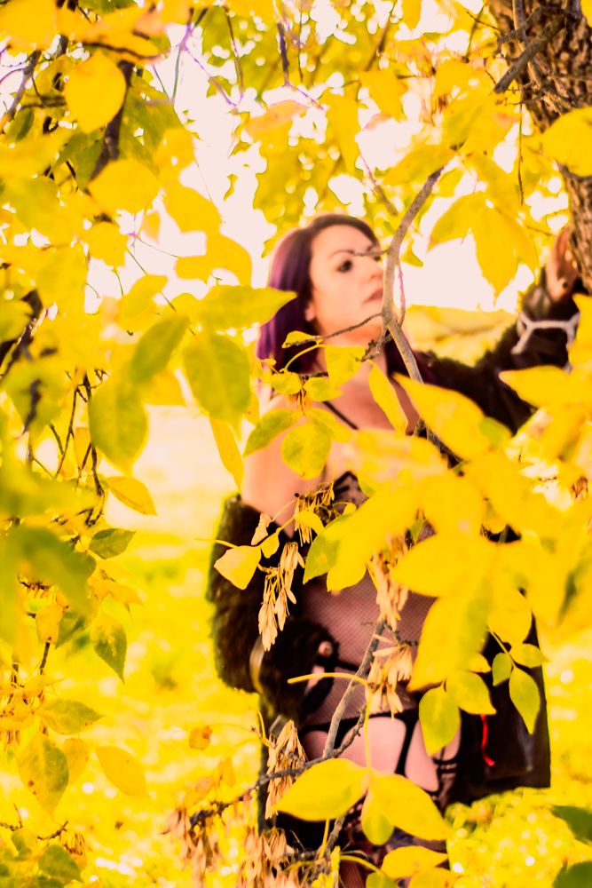 Artistic portrait among vibrant yellow autumn leaves with sheer black fishnet attire.